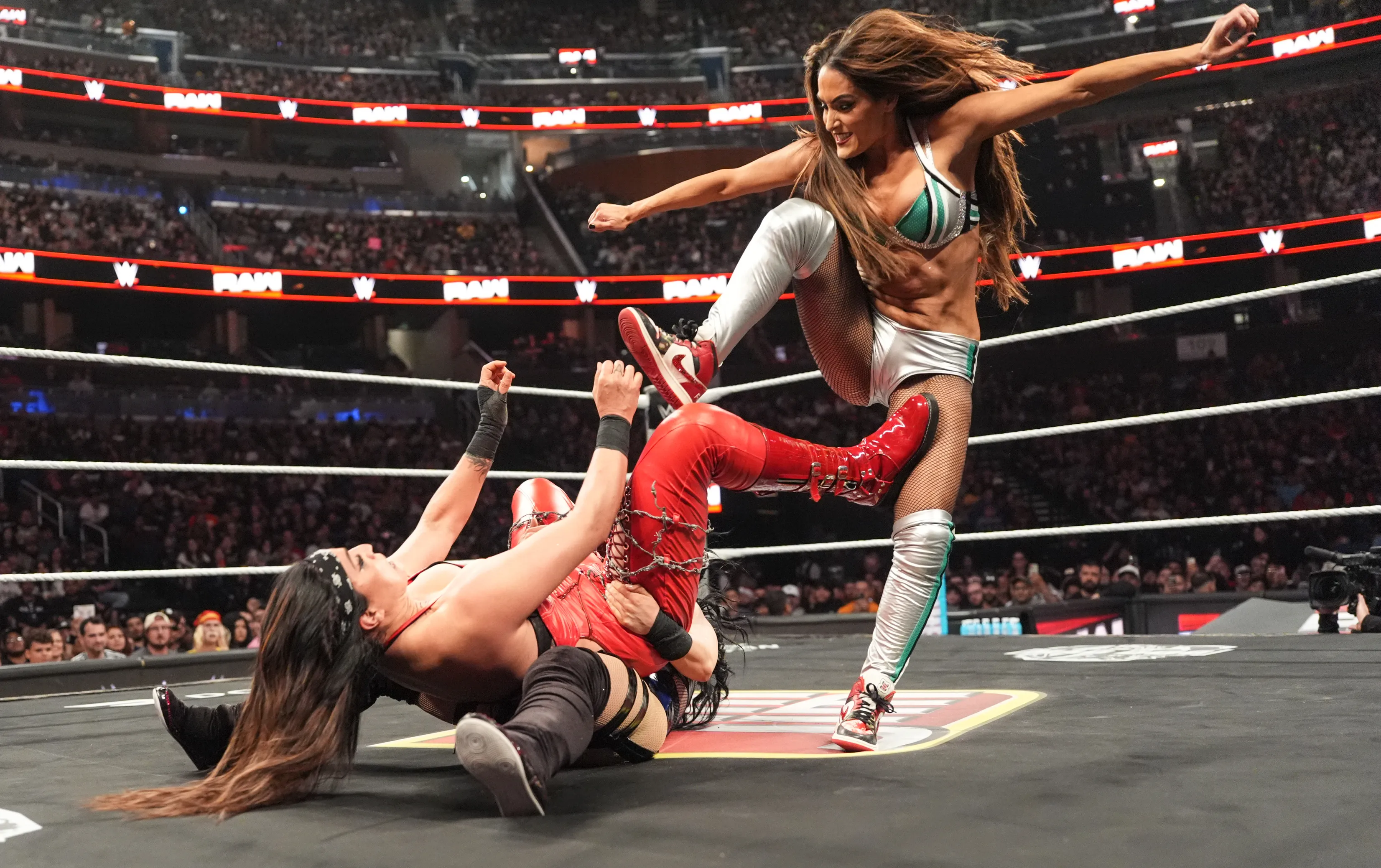 Nikki Bella delivering a kick to Raquel Rodriguez in a wrestling match.
