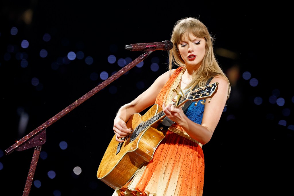 Taylor Swift performing onstage with an acoustic guitar.