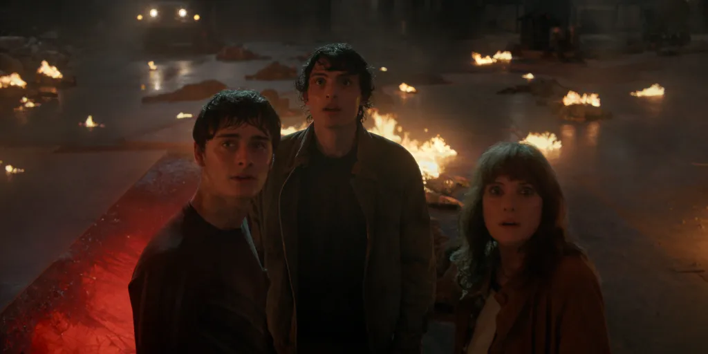 Noah Schnapp as Will Byers, Finn Wolfhard as Mike Wheeler, and Winona Ryder as Joyce Byers look up in a scene from Stranger Things: Season 5.