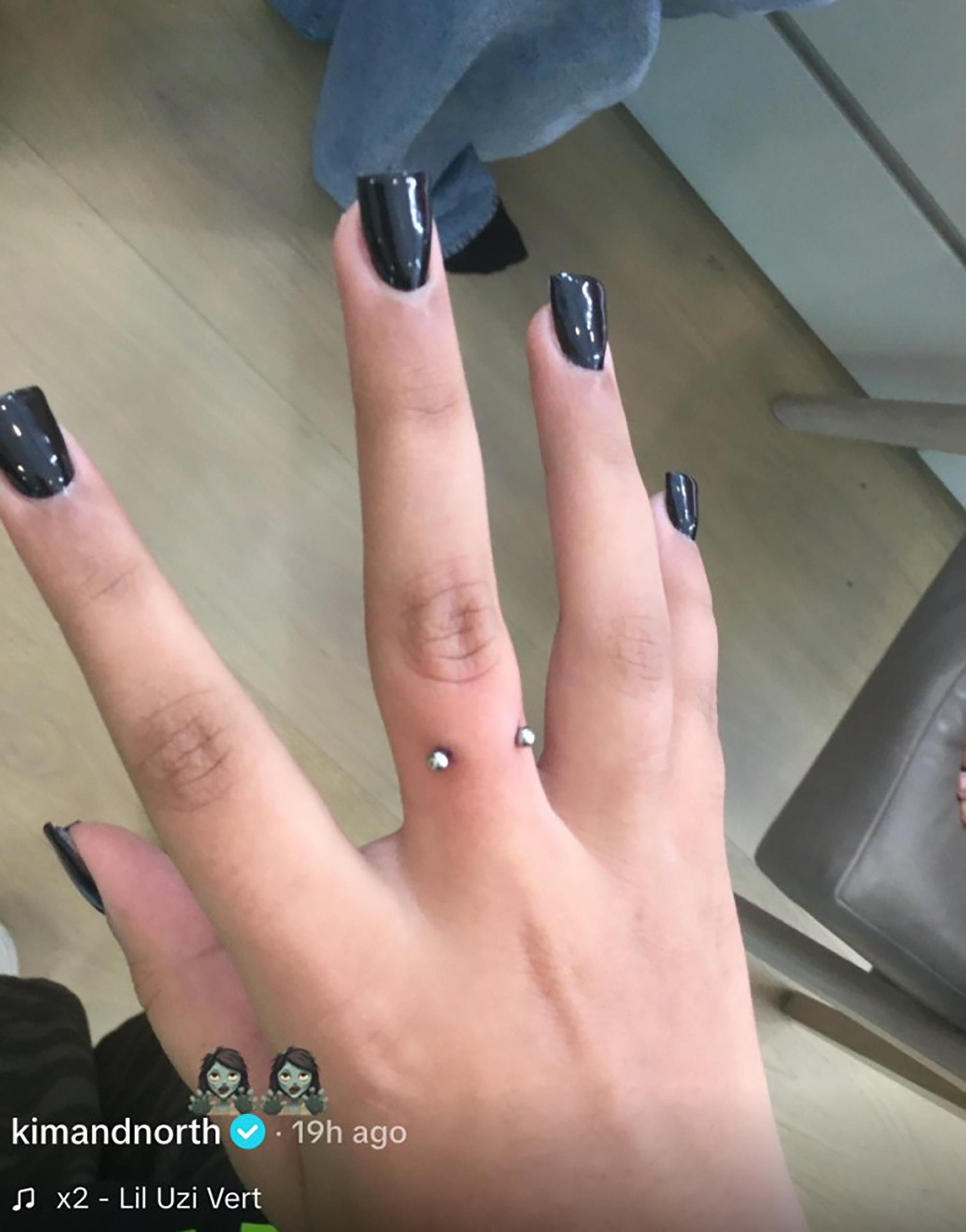 North West's hand with black nail polish and a dermal piercing.