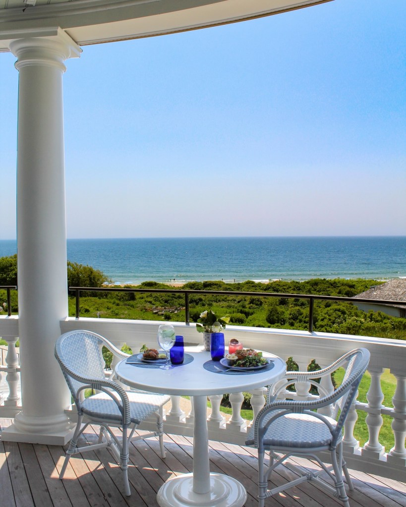 A meal for two served on a balcony overlooking the ocean.