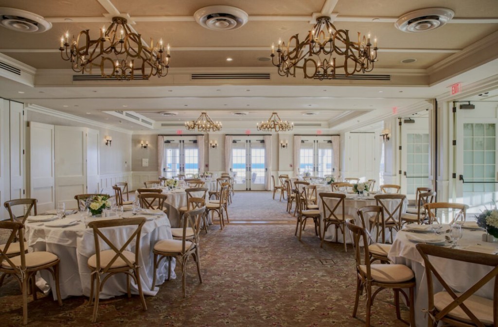 A dining hall at the Ocean House hotel in Rhode Island, set with round tables and chairs, and chandeliers.