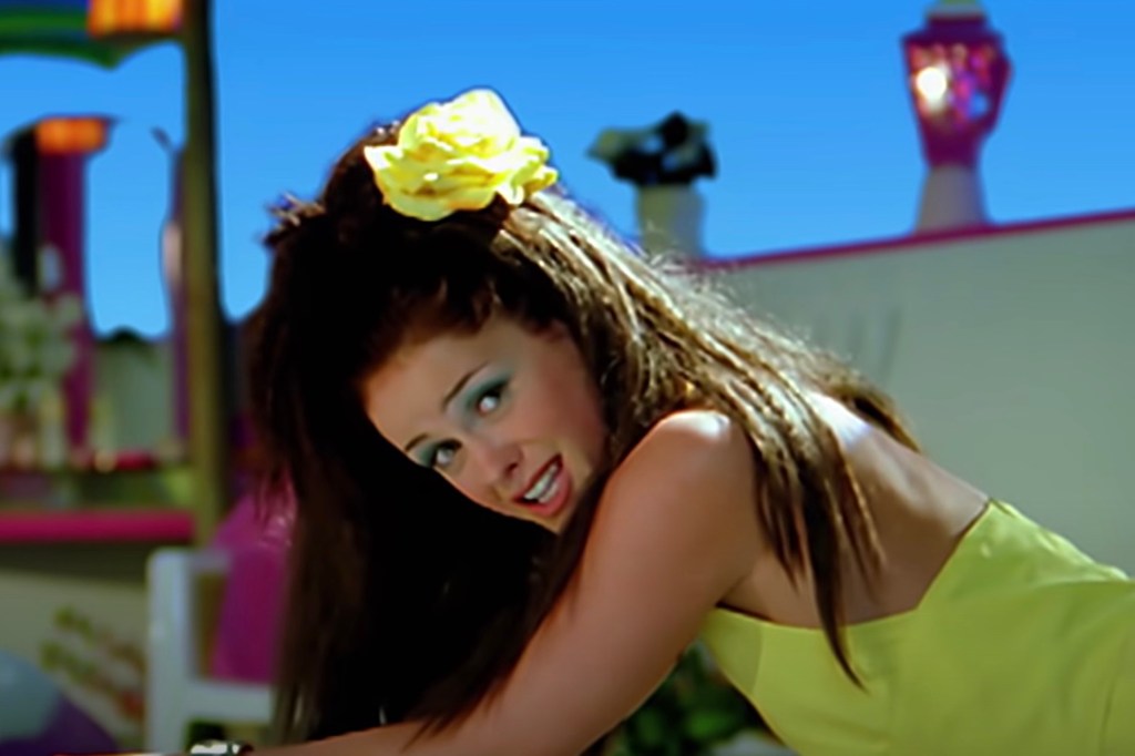 Lene Nystrøm from Aqua wearing a yellow flower in her hair and a yellow dress, looking at the camera.