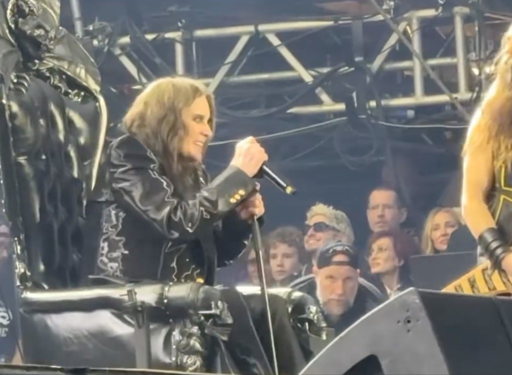 Ozzy Osbourne performing at his final Black Sabbath show while sitting in a chair, holding a microphone.