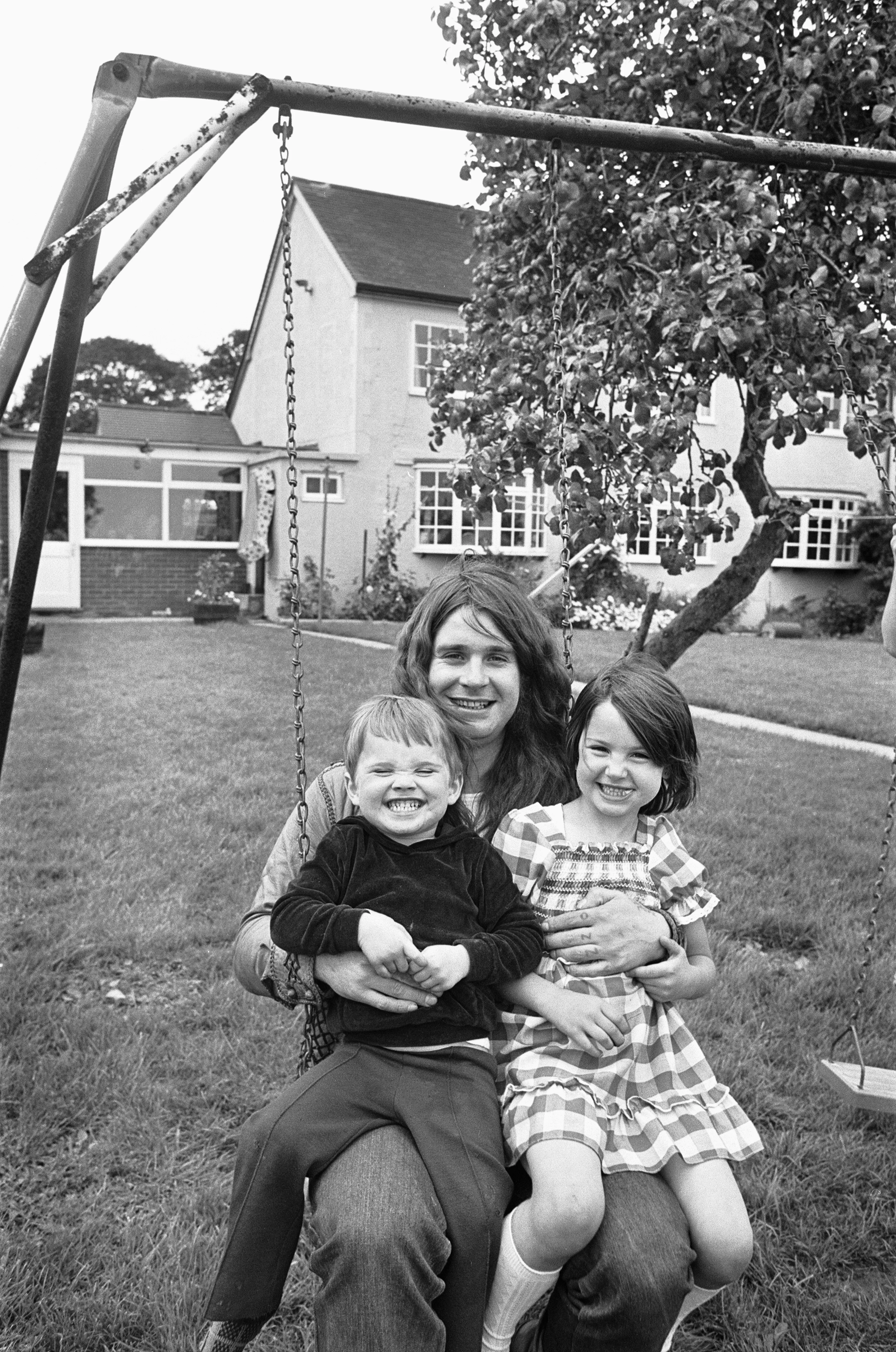 Ozzy Osbourne sitting on a swing with his two children, Jessica and Louis, at their home.