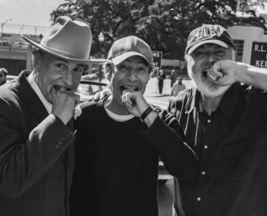 Black and white photo of three men with their fists clenched and held to their mouths.