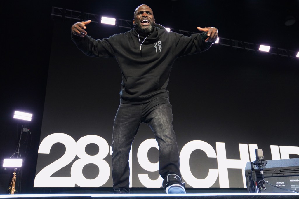 Pastor Philip Anthony Mitchell preaches with arms raised on a stage with