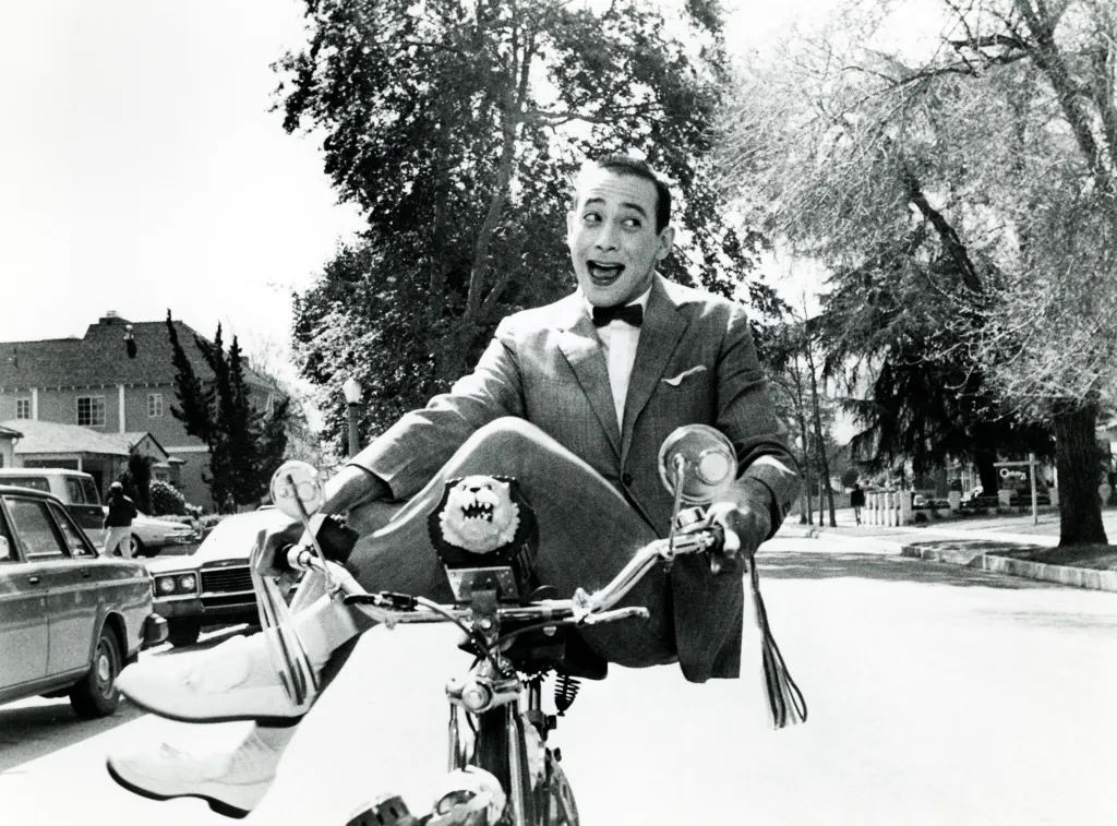 Pee-wee Herman (Paul Reubens) riding a bicycle with a startled expression.