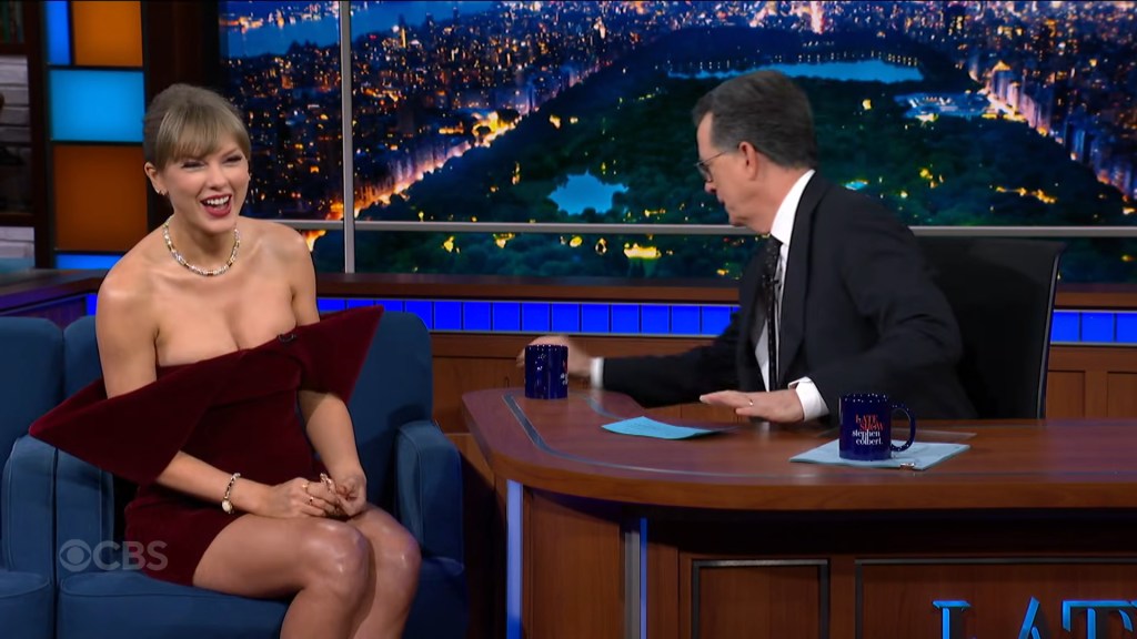 Taylor Swift smiling in a red dress with Stephen Colbert on The Late Show.