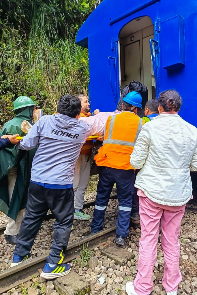 People carrying an injured passenger on a stretcher from a blue train car after a collision.