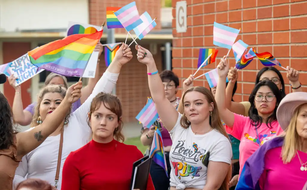 People protest against the transgender notification policy, holding transgender and rainbow flags.