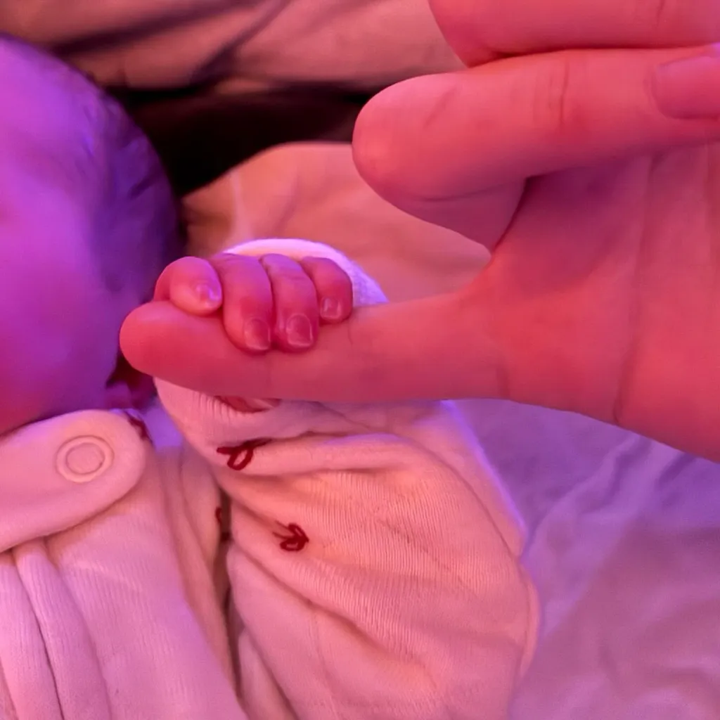 Newborn baby's hand grasping an adult's finger.