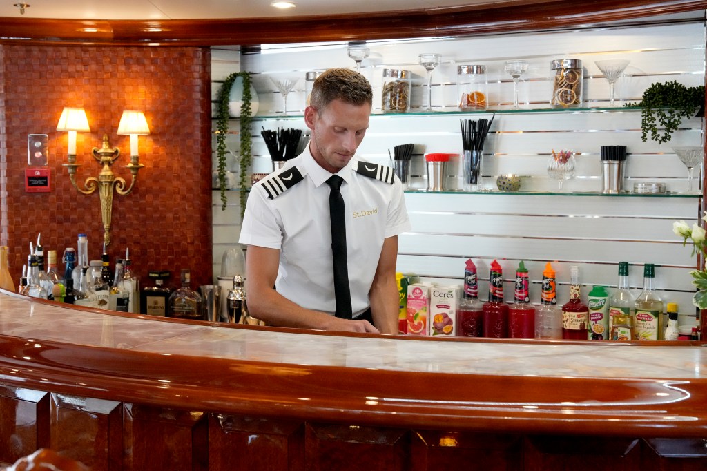 Fraser Olender from Below Deck wearing a uniform at a bar.