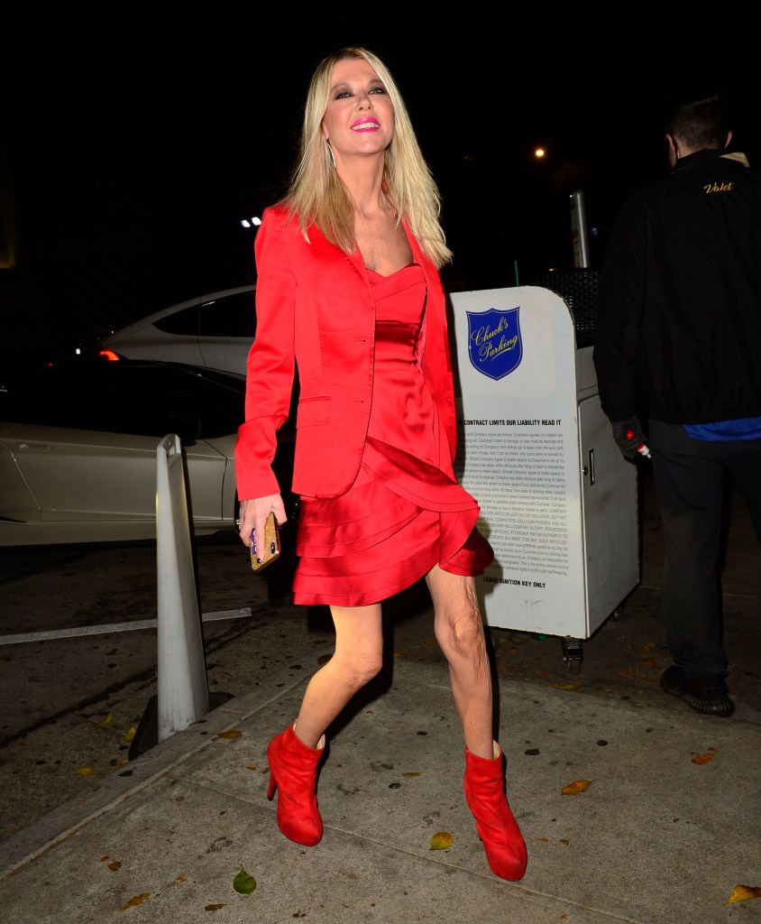 Tara Reid in a red blazer, dress, and boots, smiling at night.