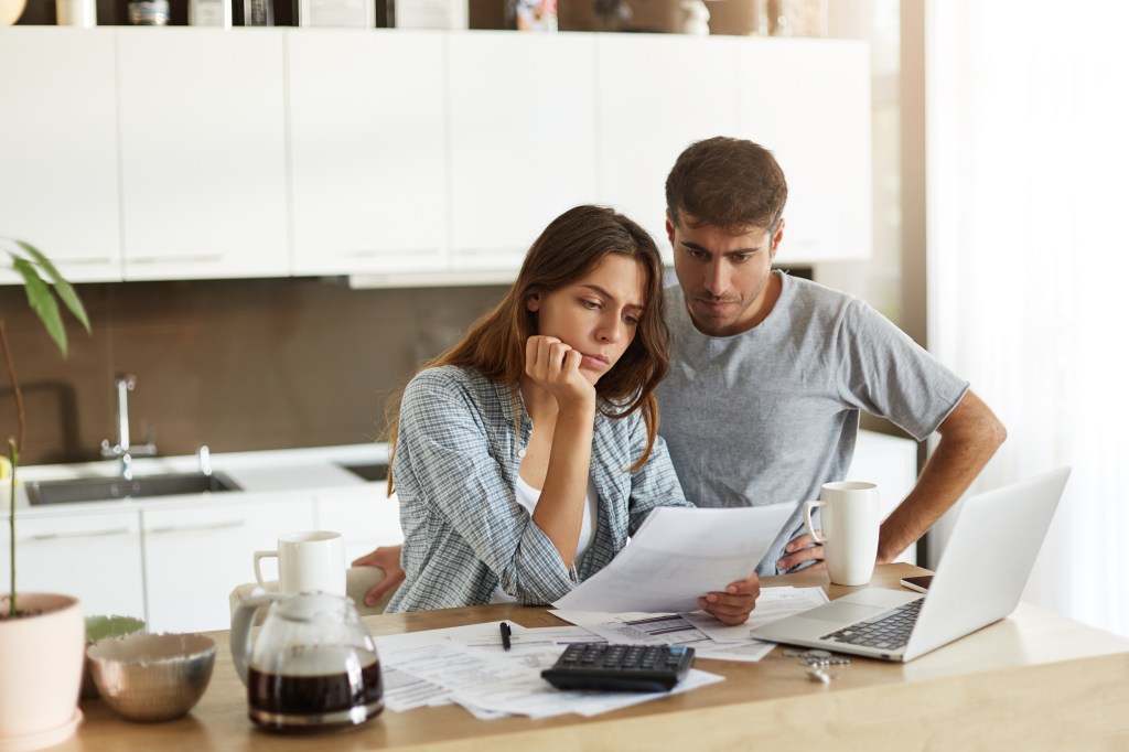 A young couple looking worried while reading financial documents in their kitchen.