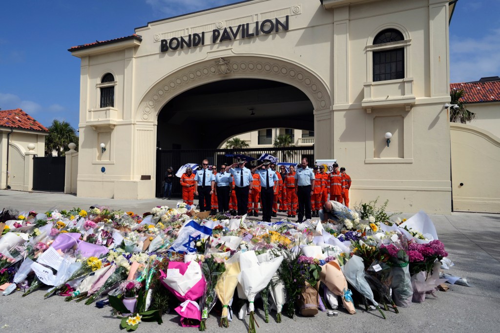 Police officers and rescue workers salute as they lay a wreath at a memorial of flowers outside the Bondi Pavilion for shooting victims.