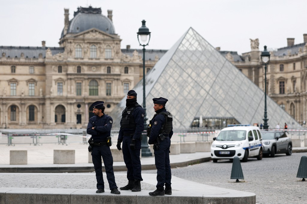 Police officers stand near the pyramid of the Louvre museum after reports of a robbery, in Paris, France, October 19, 2025.