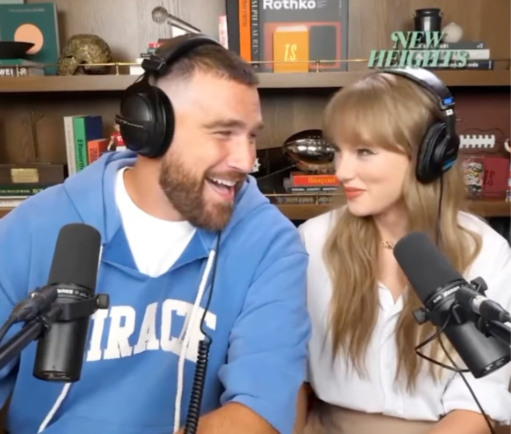 Taylor Swift and Travis Kelce wearing headphones and smiling at each other during a podcast.