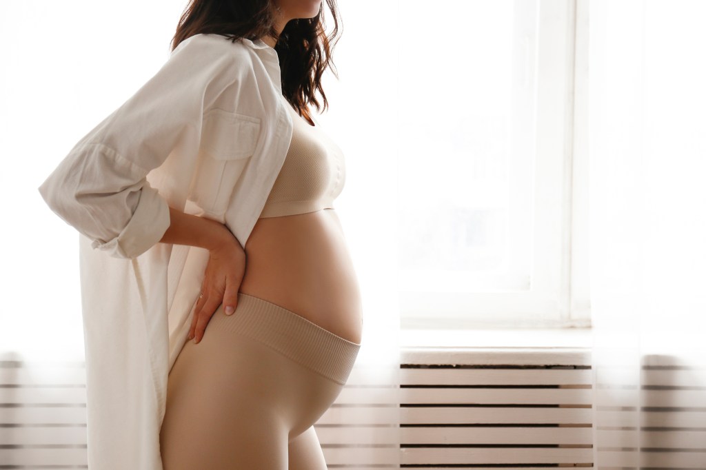 Pregnant woman in white shirt and yoga pants holding her belly.