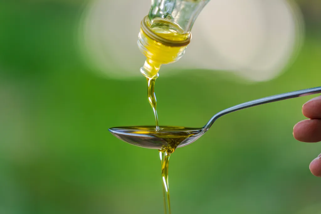 Olive oil being poured from a bottle into a spoon.