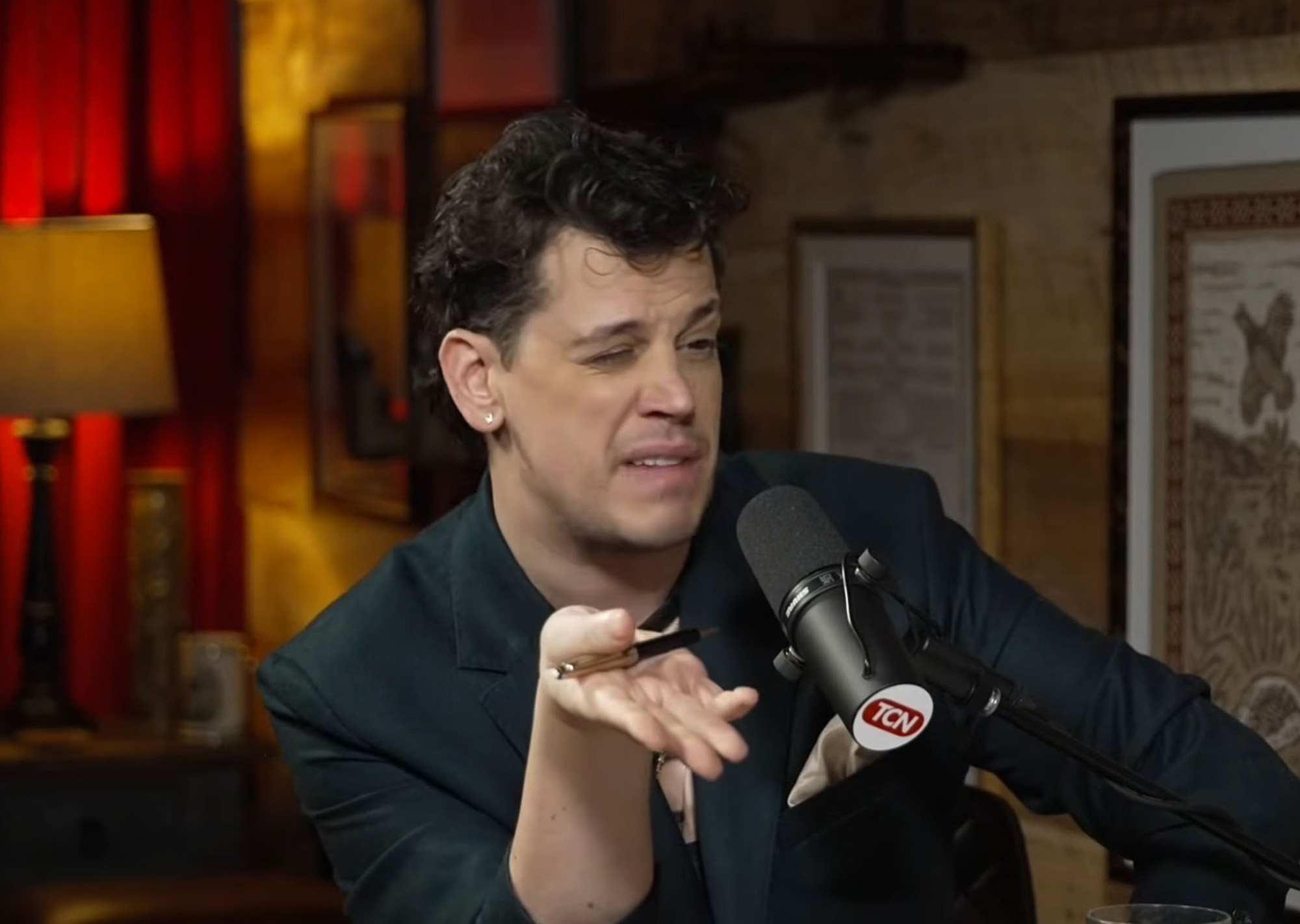 Milo Yiannopoulos on a podcast holding a pen.