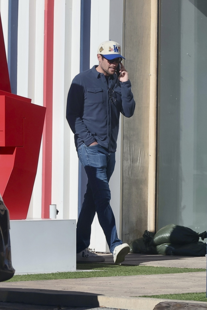 Jake Reiner in a white and blue baseball cap, blue button-up shirt, and jeans talking on his phone in Malibu.