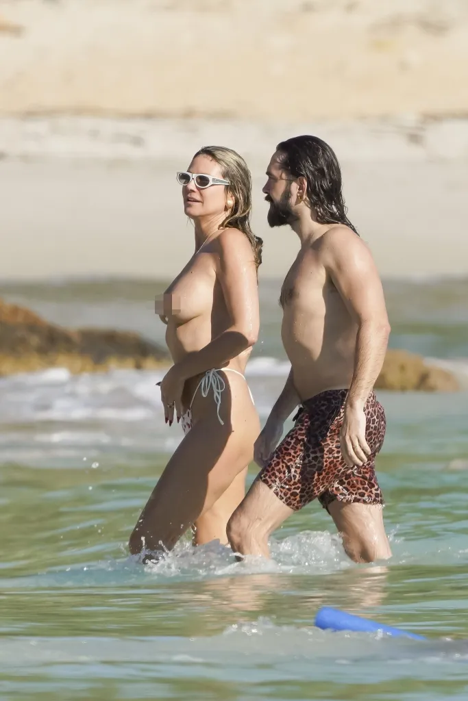 Heidi Klum, topless in a white bikini bottom, and Tom Kaulitz, in leopard print shorts, walk in the ocean during their Christmas vacation.