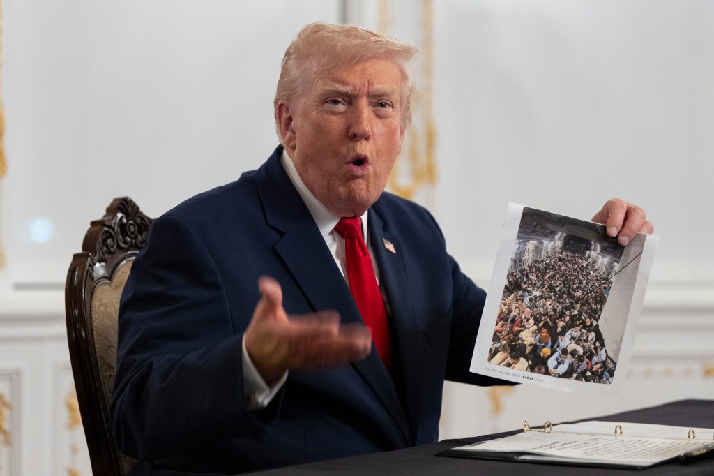 President Donald Trump holds up a photograph of migrants inside a military aircraft during Thanksgiving event at Mar-a-Lago on Nov. 27, 2025.
