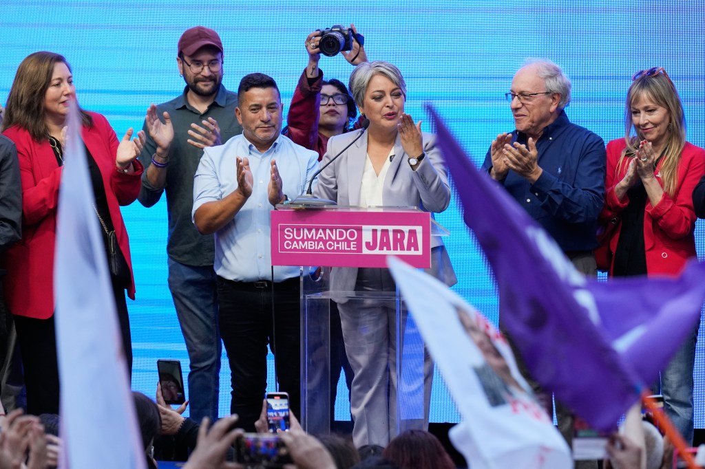 Presidential candidate Jeannette Jara blows a kiss to supporters after conceding the election, with other people clapping behind her.