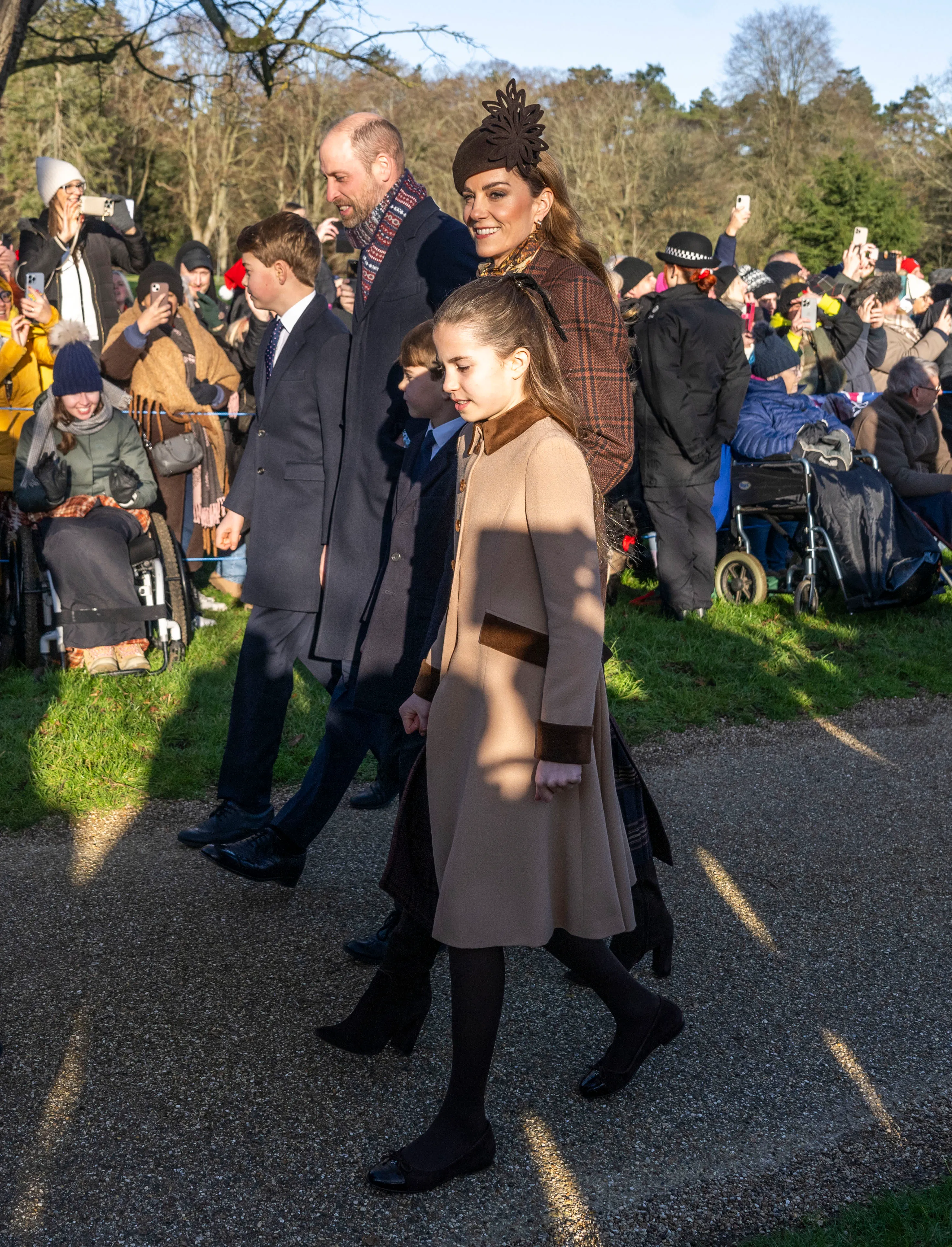 Prince William, Princess Catherine, Prince George, Princess Charlotte, and Prince Louis walking outdoors with crowds of people behind them.