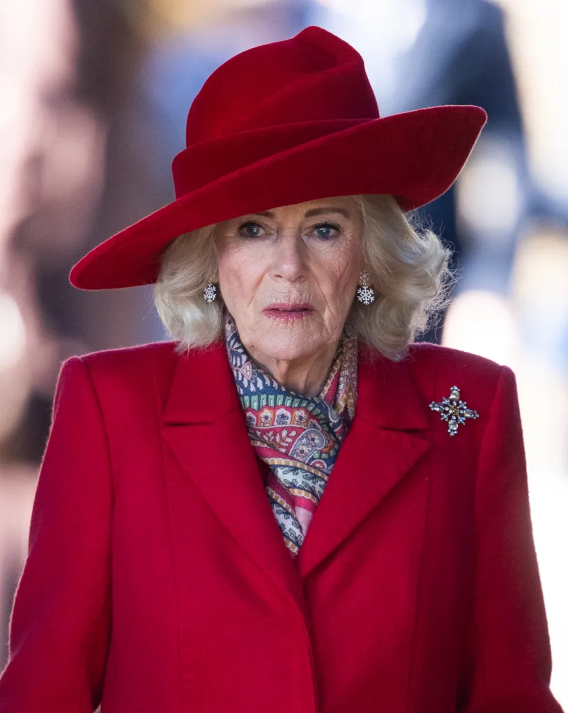 Queen Camilla wearing a red hat and coat with a patterned scarf and snowflake earrings.