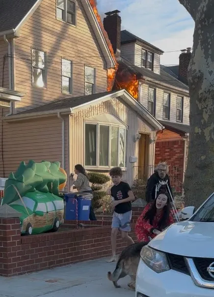 People watch as a house in Queens burns.
