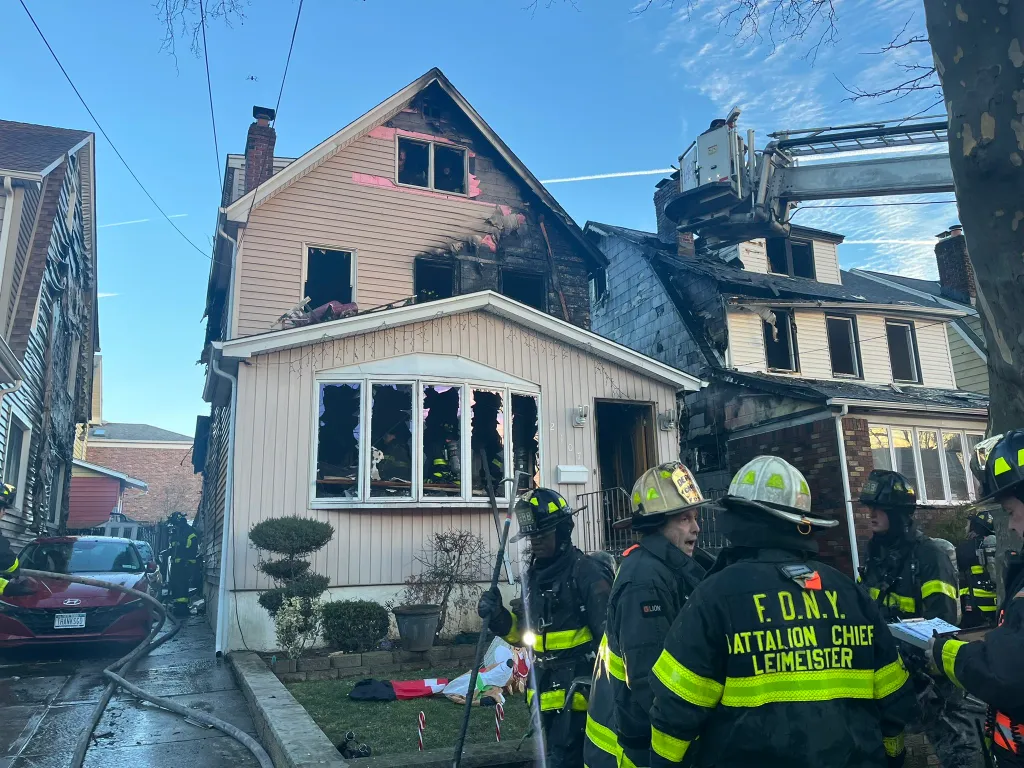 Firefighters on the street and in an aerial ladder battling a house fire in Queens, New York.