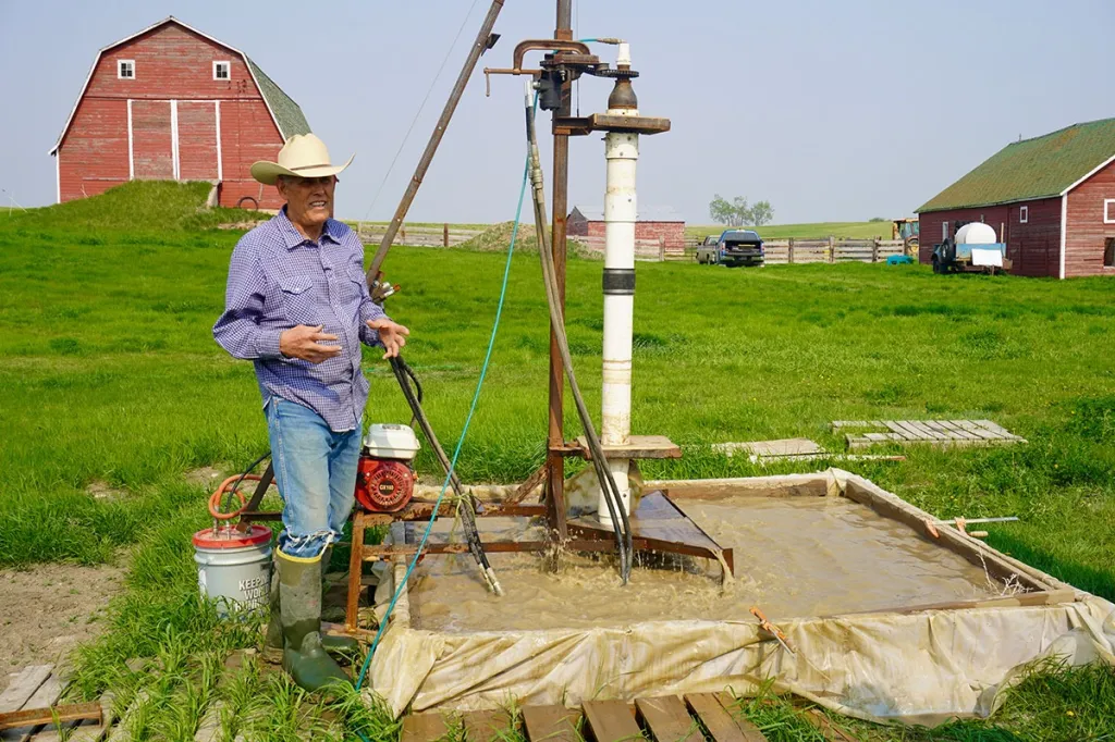 Rancher explaining a portable water well drilling rig and mud pit.