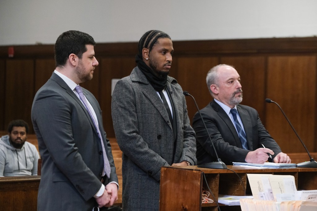Rapper Trey Songz in court, wearing a gray coat, black scarf, and braids, standing between two men in suits.