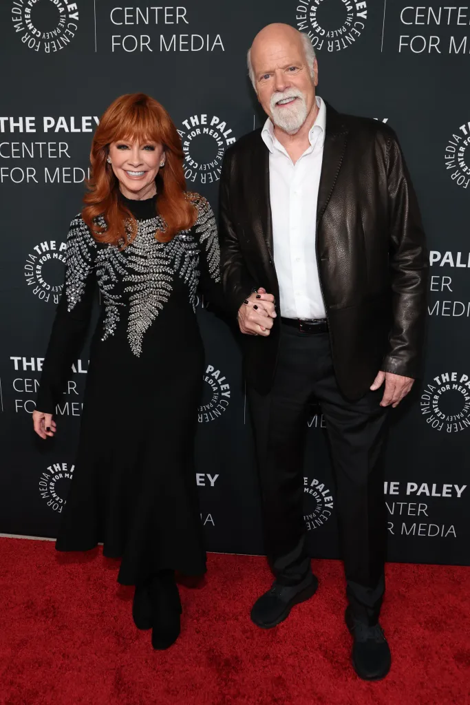Reba McEntire and Rex Linn holding hands on a red carpet.