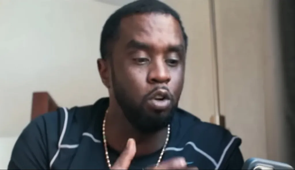 Sean Combs speaking, wearing a dark blue shirt and a gold chain.