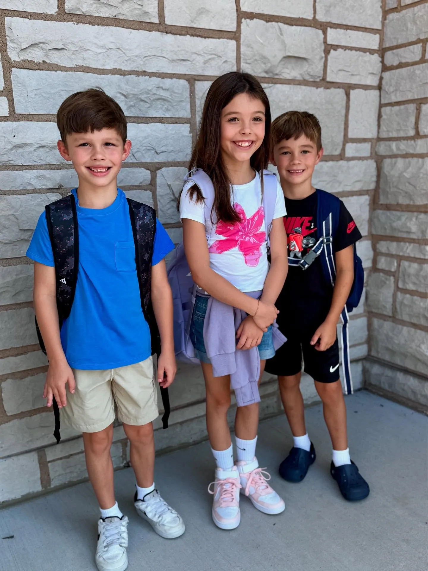 Meghan King's children, two boys and a girl, standing with backpacks.