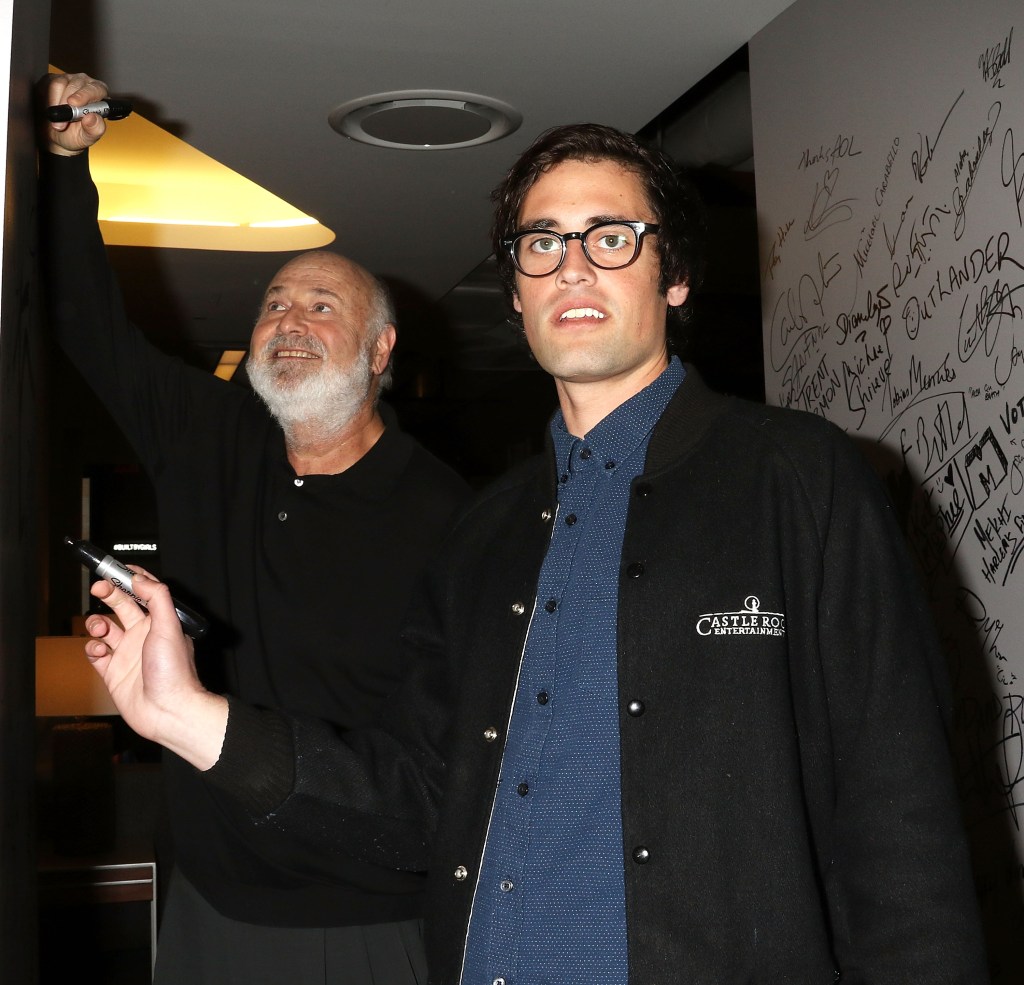 Rob Reiner and Nick Reiner signing a wall with other autographs.
