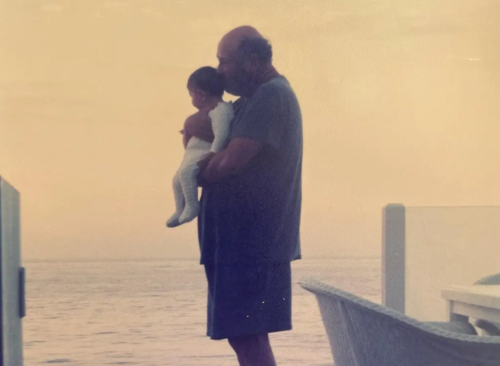 Rob Reiner holding Romy Reiner as a baby by the ocean.