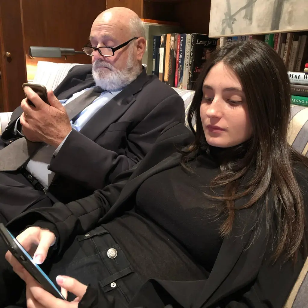 Rob Reiner and Romy Reiner sitting and looking at their phones.