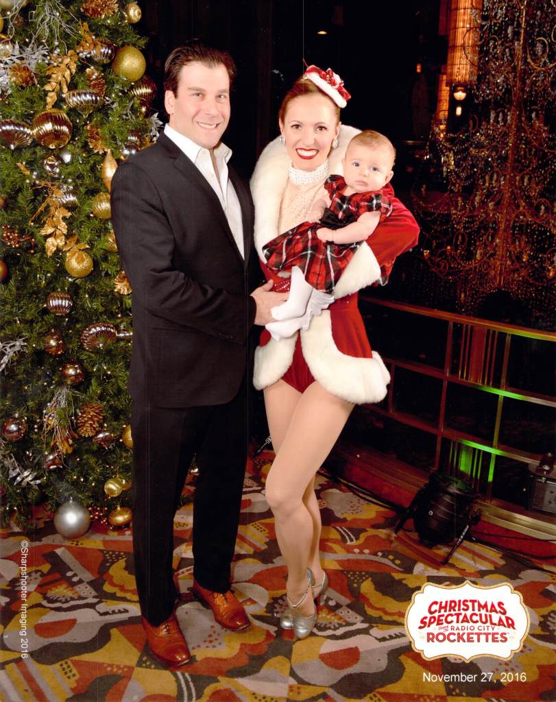 Rockette Alina Silver and her husband Geoff holding their baby Amanda in front of a Christmas tree at Radio City Music Hall.