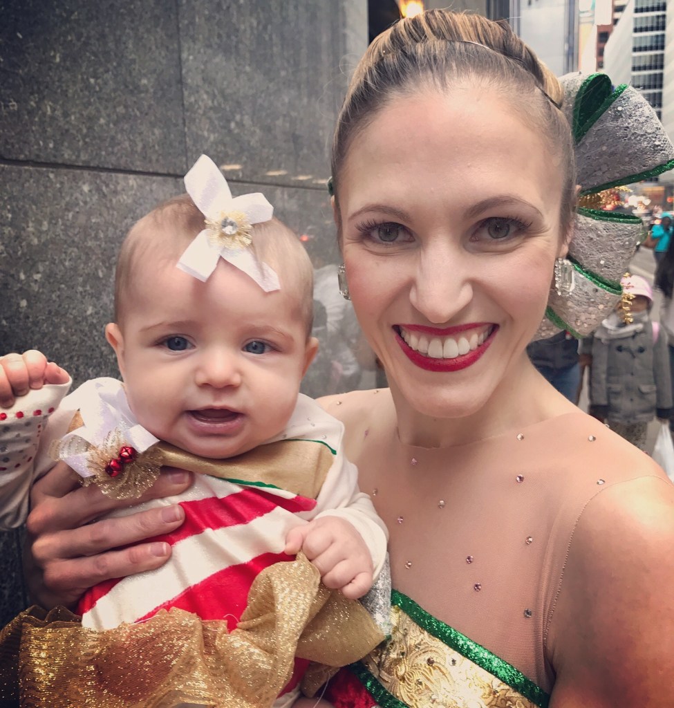 Rockette Alina Silver holding her baby Amanda who is dressed in a Christmas-themed outfit ar Radio City