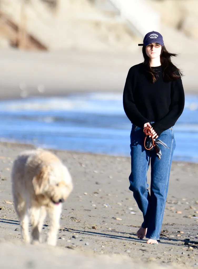 Romy Reiner barefoot on a sandy beach with a dog.