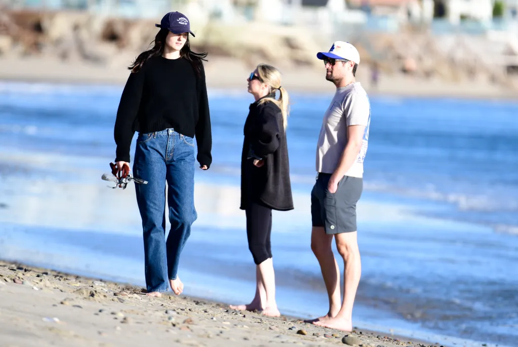 Romy Reiner and Jake Reiner walking barefoot on a beach with Jake's girlfriend and a friend.