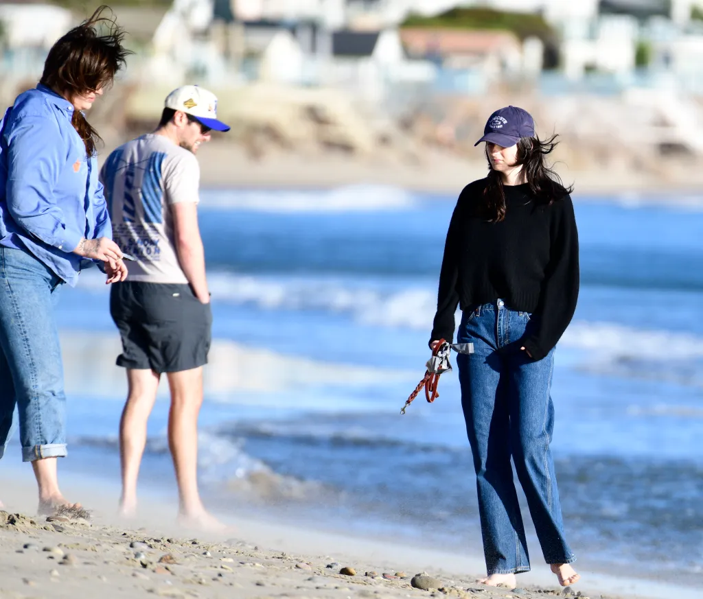 Romy Reiner and Jake Reiner walking barefoot on a beach with a friend.