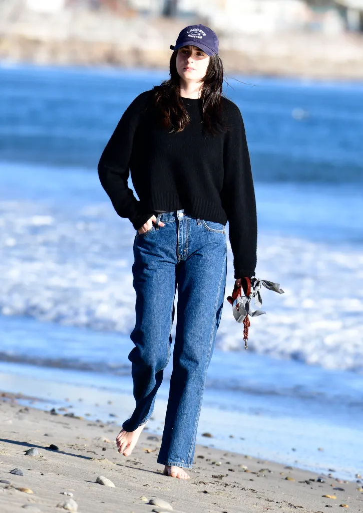 Romy Reiner walking barefoot on a beach, holding a dog leash.