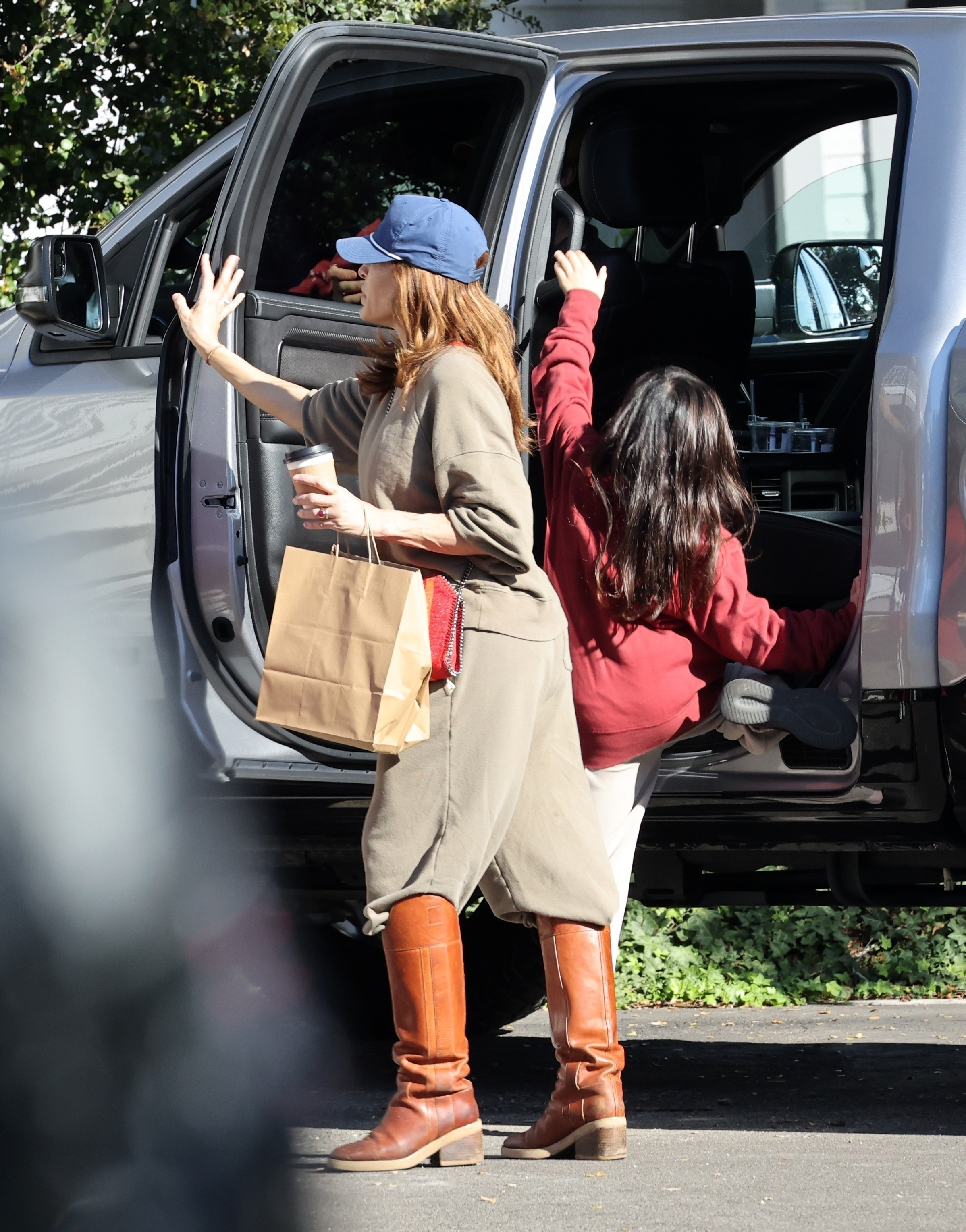 Eva Mendes helping her daughter into a car with shopping bags and coffee.