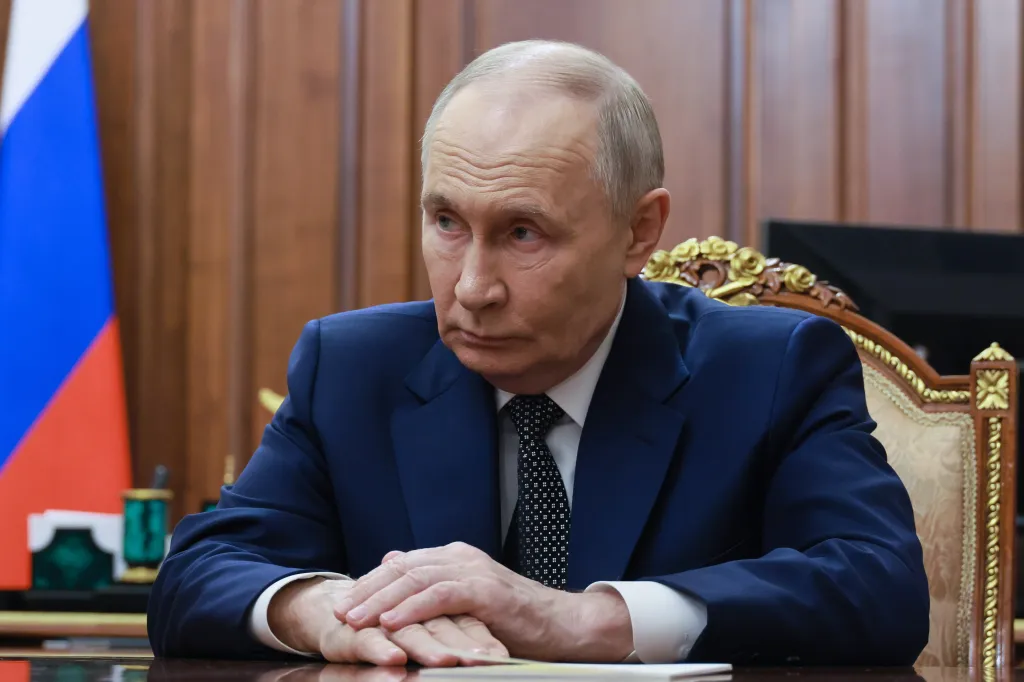 Russian President Vladimir Putin in a dark suit with hands clasped on a table.