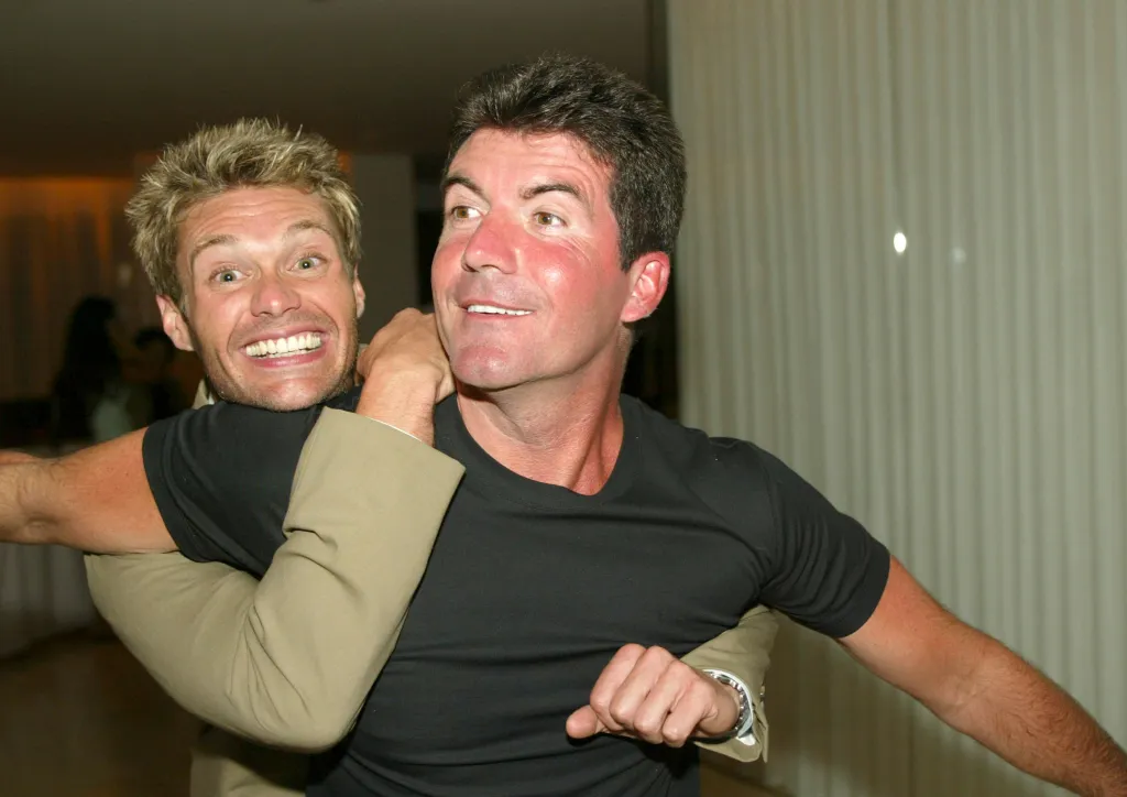 Ryan Seacrest with his arm wrapped around Simon Cowell's neck and shoulder.